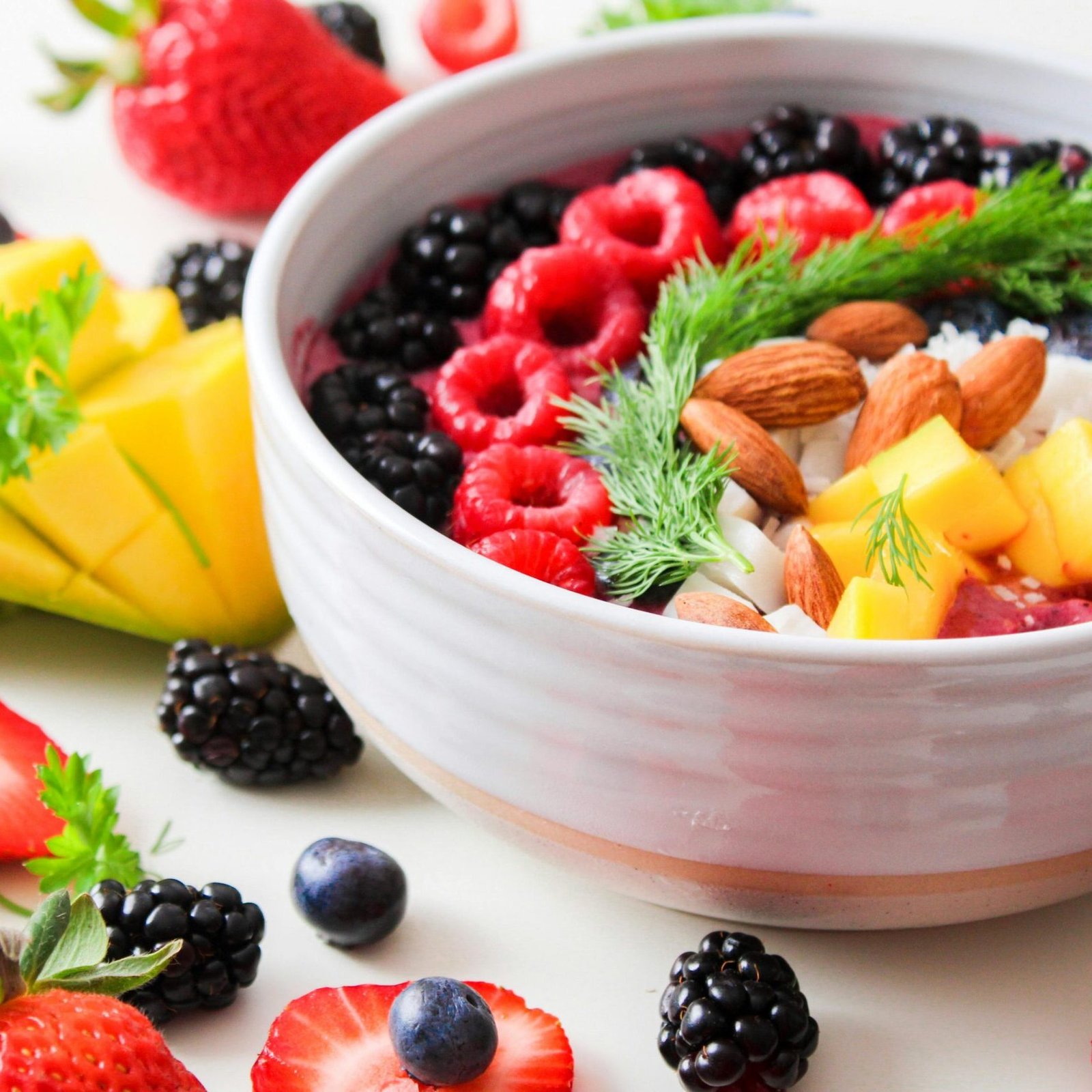 A vibrant bowl filled with fresh berries, mango, almonds, and herbs, perfect for a healthy snack or breakfast.