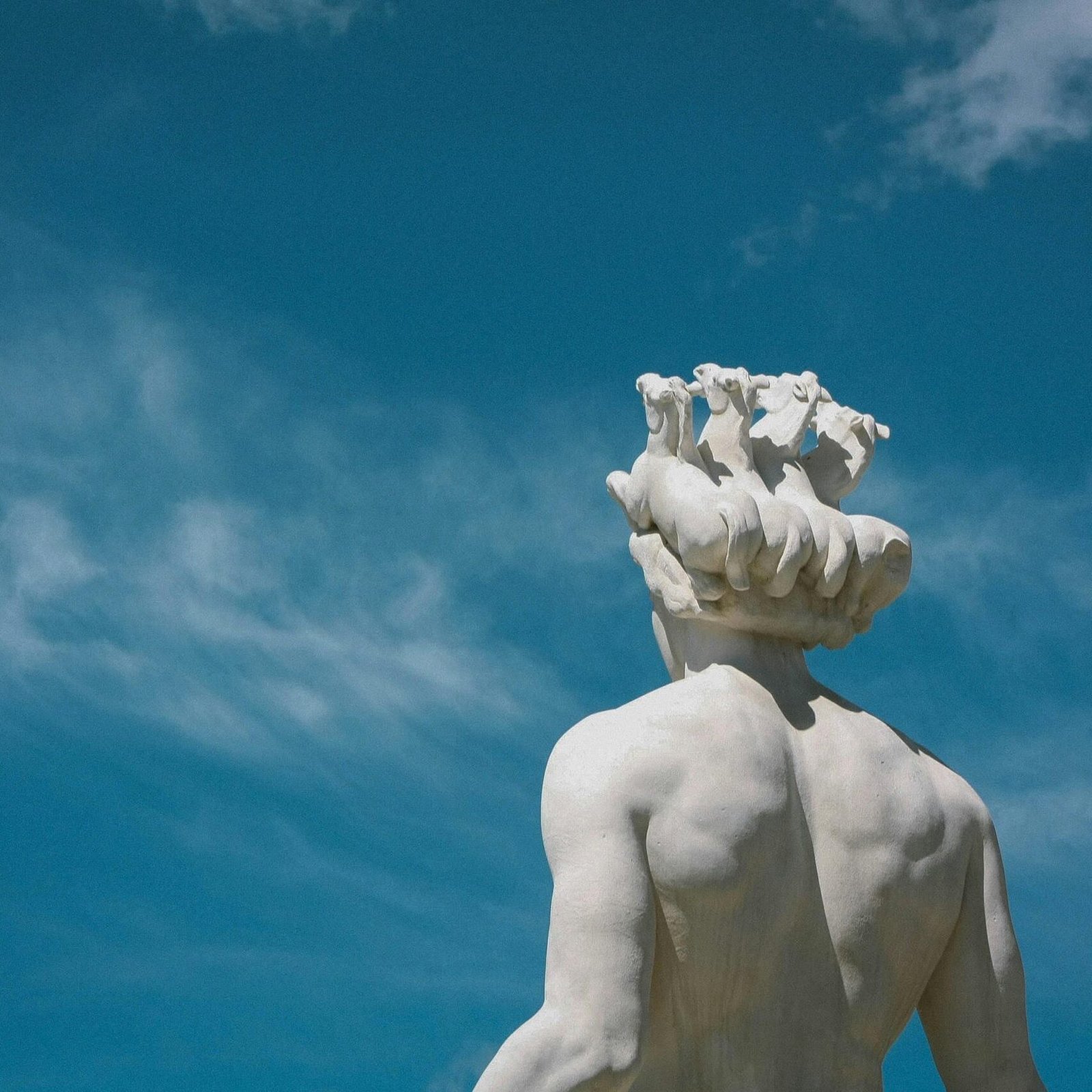 Low-angle view of a Greek statue on a sunny day with a clear blue sky.