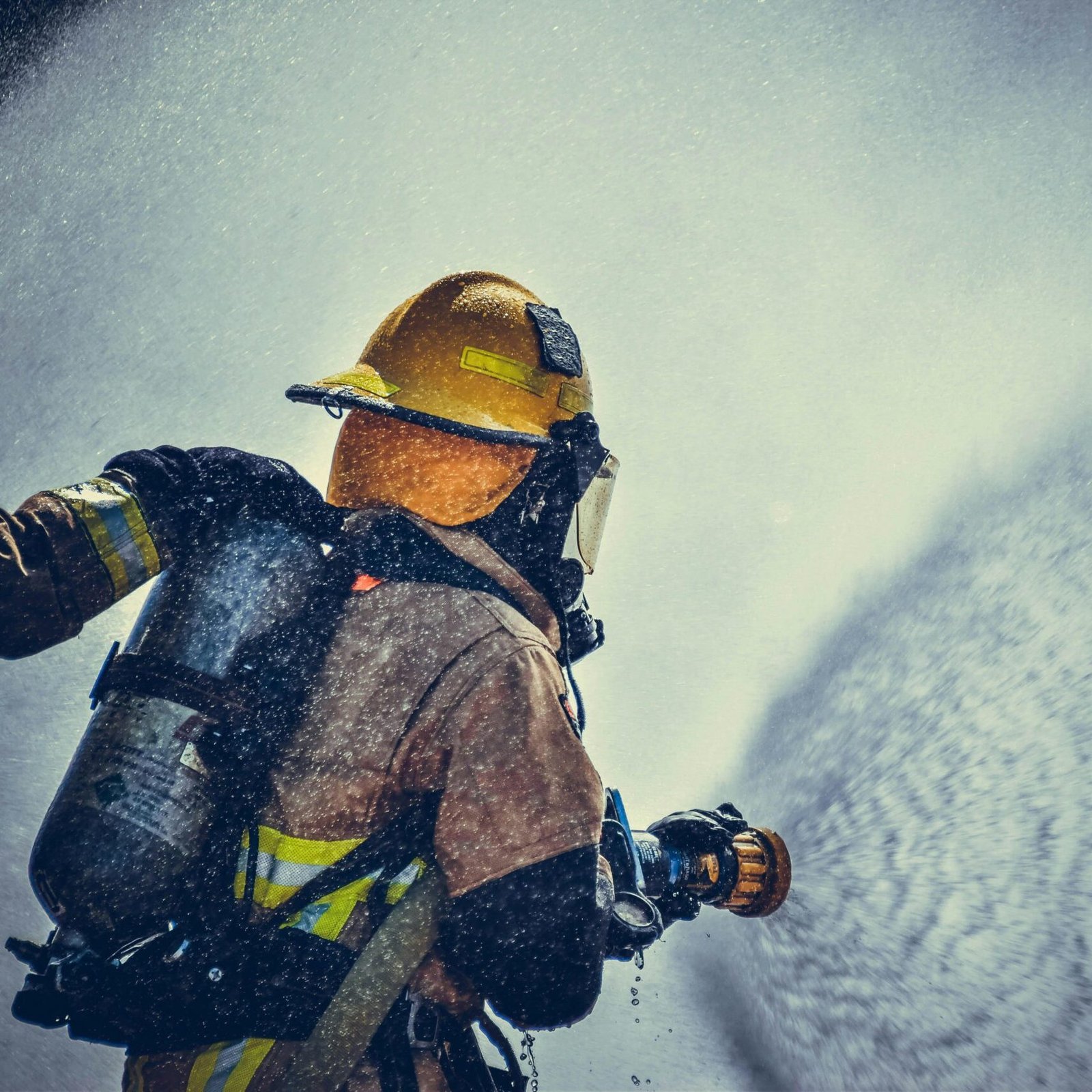 A brave firefighter in protective gear sprays water during training or emergency.