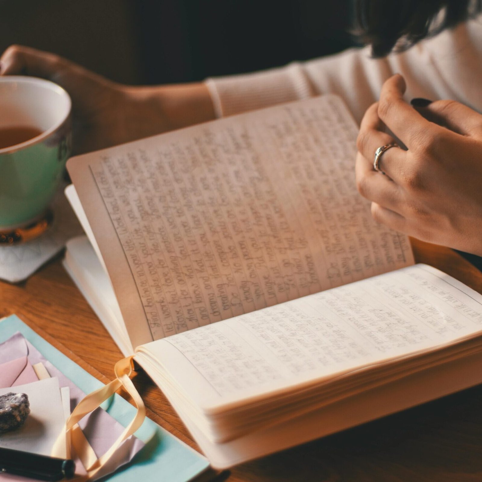 A woman writes in a journal while enjoying a cup of coffee at a wooden table.