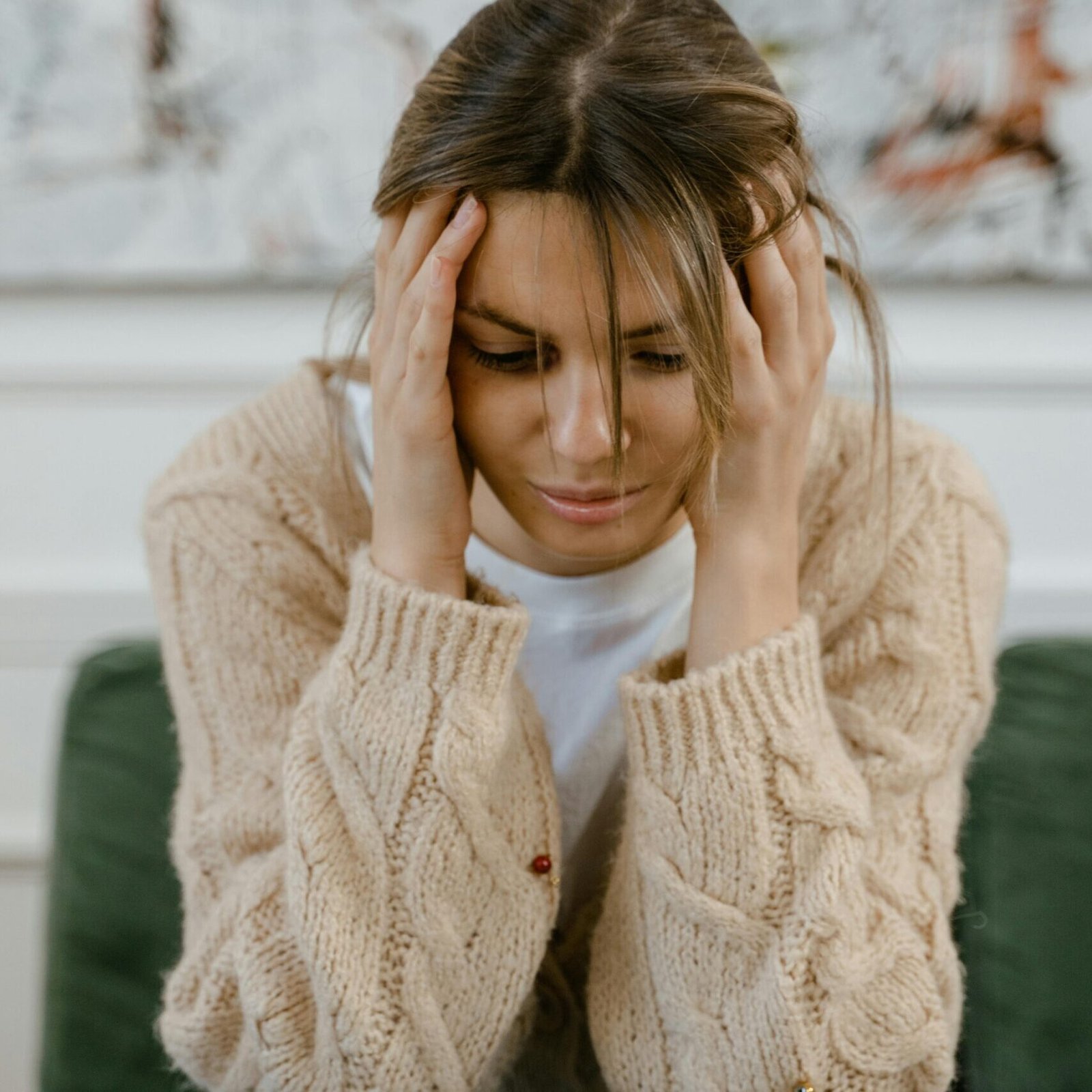 A woman sitting on a sofa holding her head, expressing stress and frustration indoors.