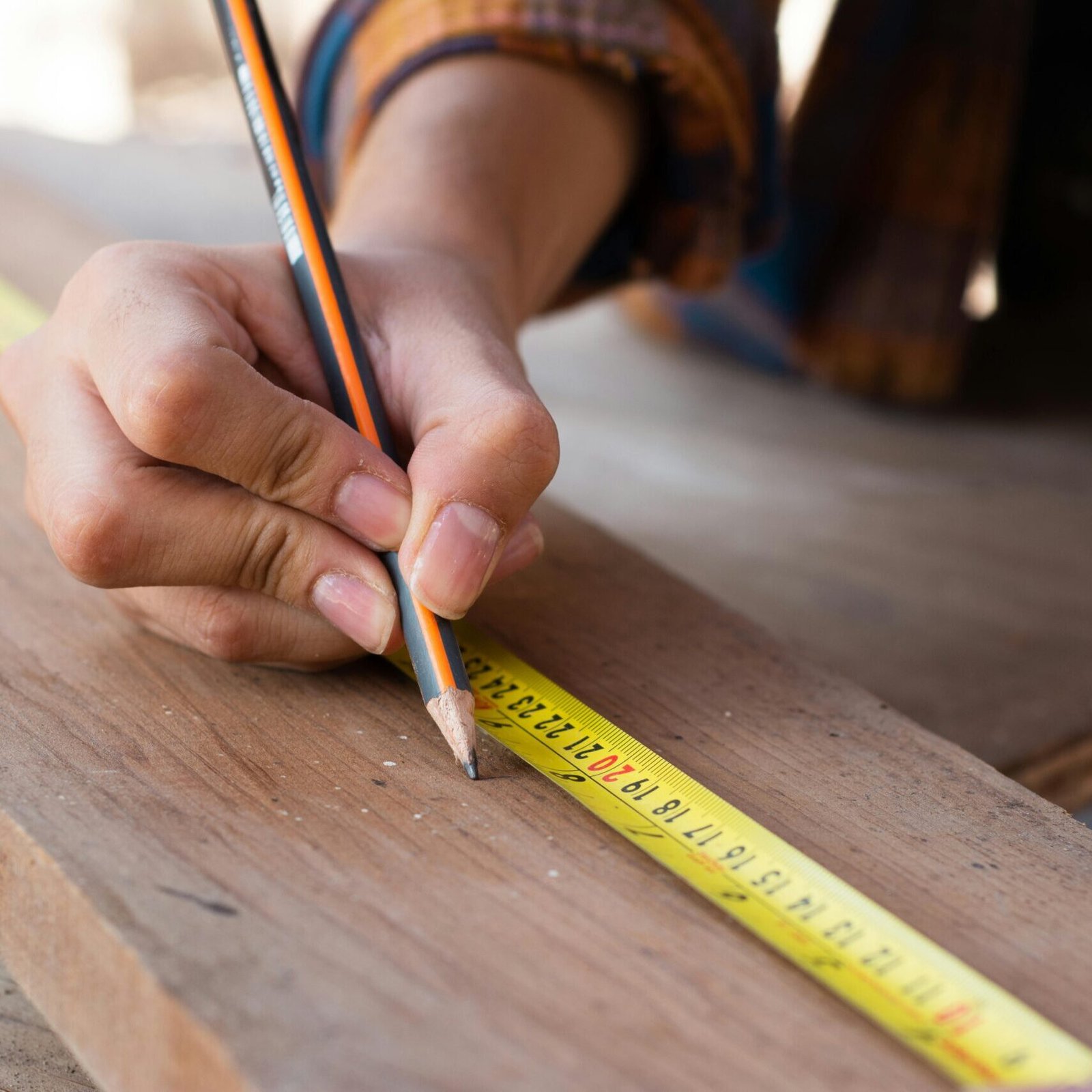 Close-up of hands using a measuring tape and pencil, highlighting precision in carpentry work.